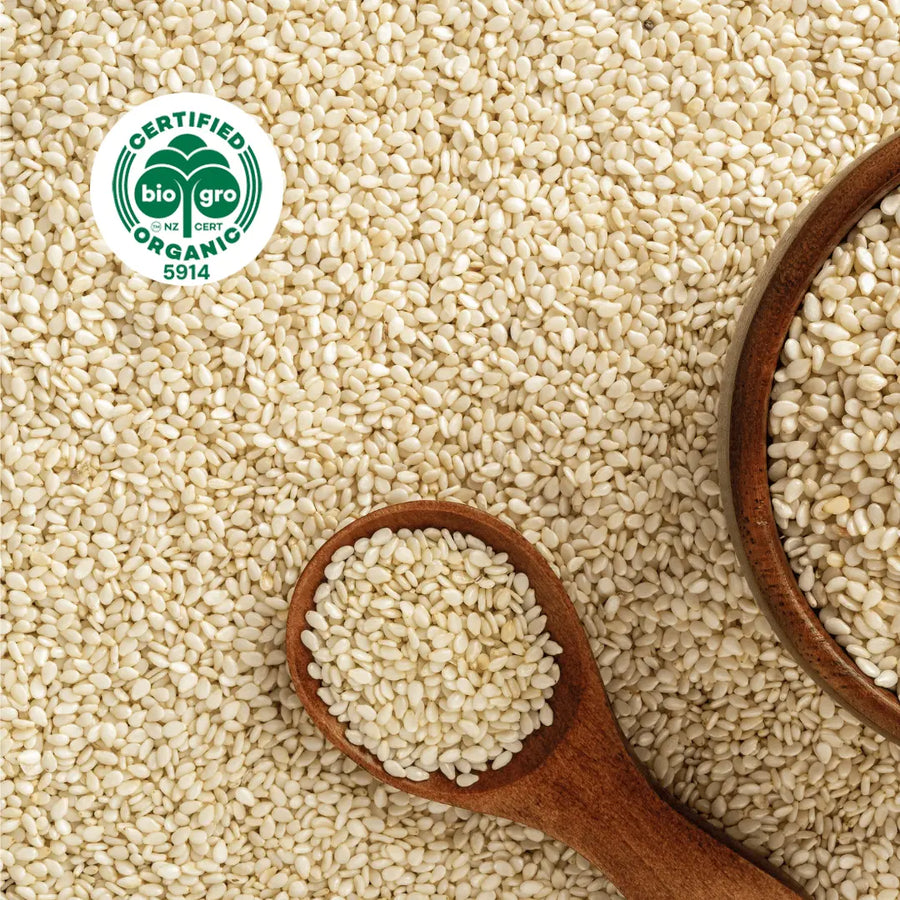 small white sesame seeds surrounding and inside of a wooden spoon and bowl with BioGro Certified Organic icon to verify Go Native New Zealand's organic certification for sesame carrier oil