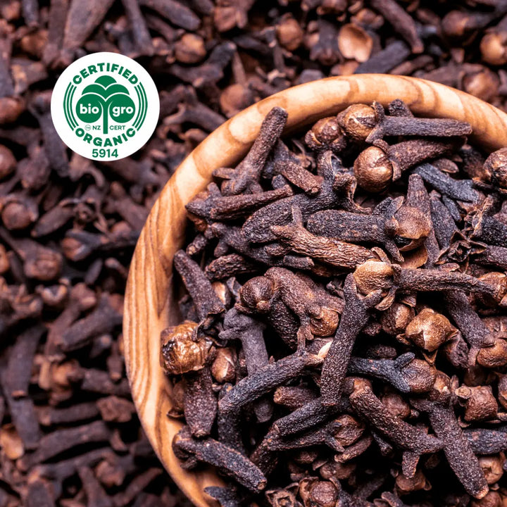 Golden red brown Clove buds in bowl and surrounded for making Go Native NZ Essential Oil with Bio Gro sticker verifying Certified Organic 