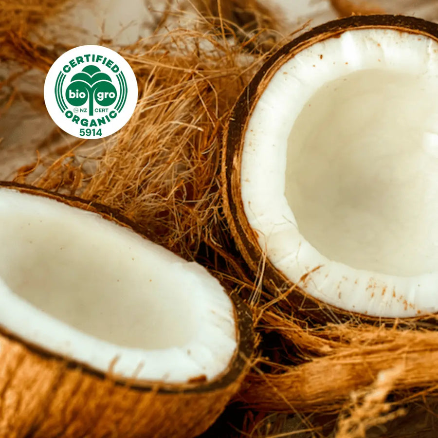 coconut in husk split open to reveal white coconut meat inside with bio gro Certified Organic icon to verify Go Native New Zealand's organic certification for RBD coconut carrier oil
