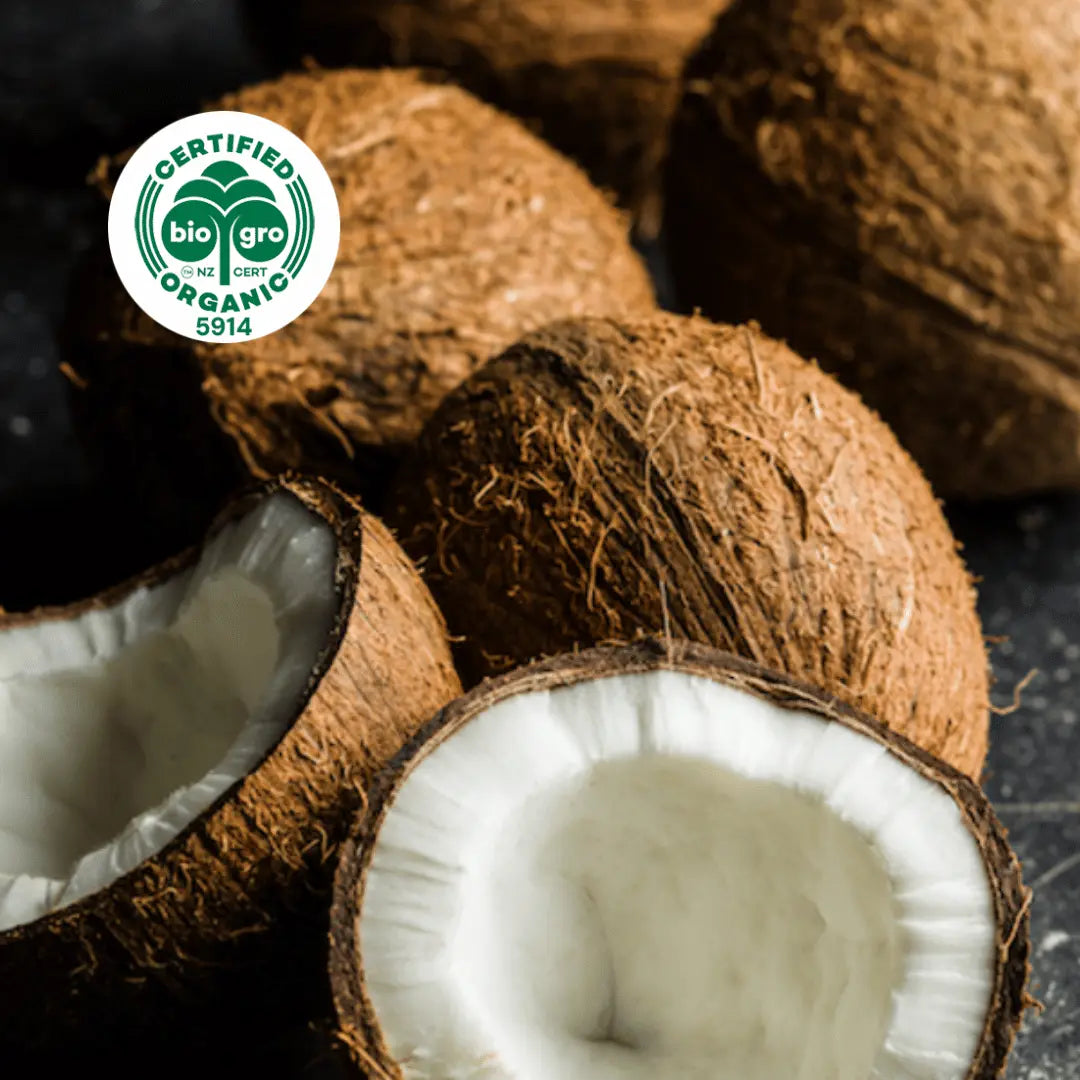 coconuts whole in shells and also split open to reveal white coconut meat inside with bio gro Certified Organic icon to verify Go Native New Zealand's organic certification for virgin coconut carrier oil