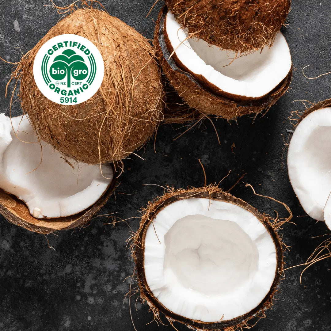 Coconuts split open to reveal white coconut flesh inside with bio gro Certified Organic icon to verify Go Native New Zealand's organic certification for fractionated coconut carrier oil