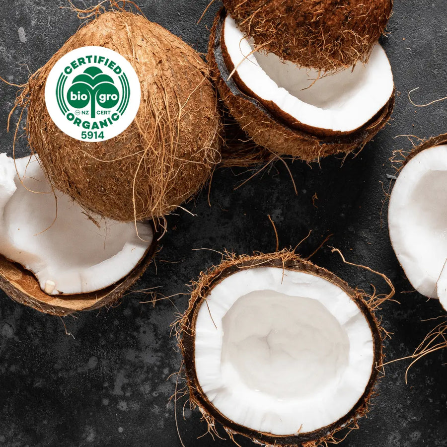 Coconuts split open to reveal white coconut flesh inside with bio gro Certified Organic icon to verify Go Native New Zealand's organic certification for fractionated coconut carrier oil