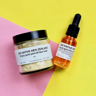 Two Go Native products Liquid gold skin replenishing serum on bottle and Peel off gold mask in jar on bright pink and yellow card