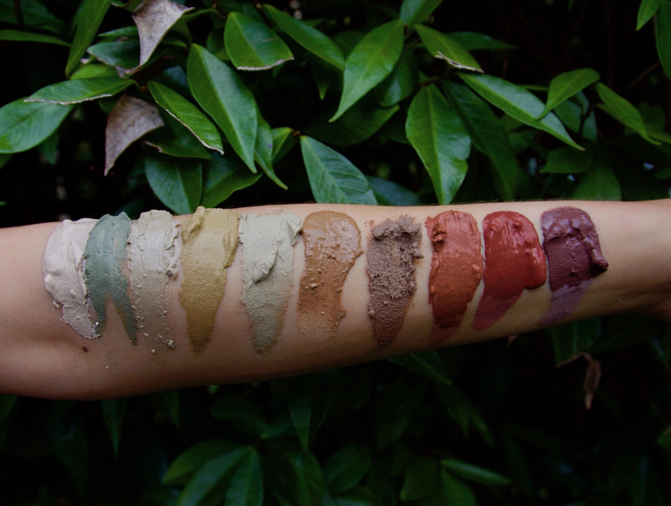 Swatches of naturally coloured clays on a person's arm with a natural leafy background